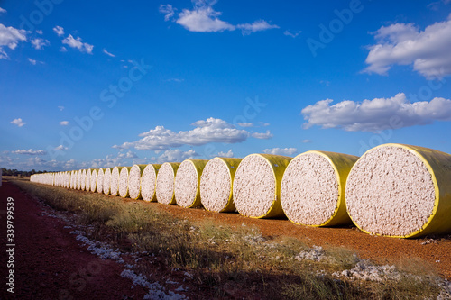 Row of yellow wrapped cotton bales against a blue sky with clouds.