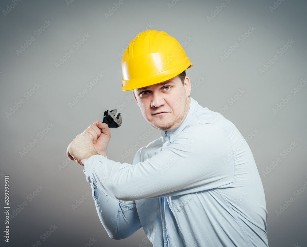 Smiling young mechanic in boiler suit with wrench and arms folded Smiling young mechanic in boiler suit with wrench and arms folded