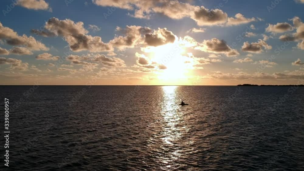 Silhouette of person kayaking in the ocean during sunset, aerial orbiting left Silhouette of person kayaking in the ocean during sunset, aerial orbiting left