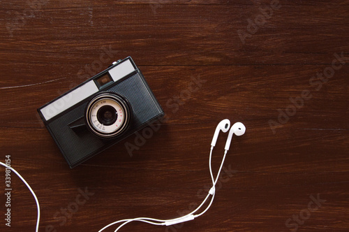 Retro old camera with white headphones on dark brown wooden background, top view. Old fashion film camera. 