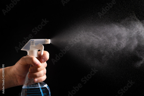 On a black background, a Hand with a spray bottle. A spray of water. Antibacterial gel for hand disinfection.