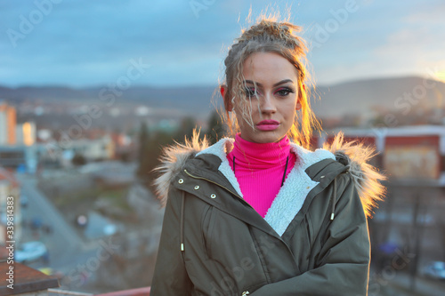 Side view of a beautiful girl watching the sunset from the building. A beautiful blonde young female lady enjoying the cityscape and amazing sunset with colorful bright sunset sky . Tourism traveling.