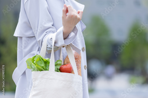 スーパーマーケットで買物した食品をエコバッグに入れてもつ若い女性の手元 photo