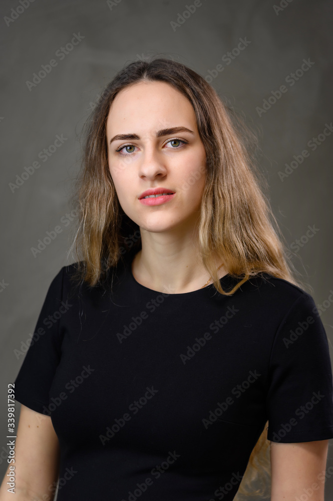 Vertical portrait of a caucasian girl in a black dress with long hair on a gray background. Vertical portrait of a caucasian girl in a black dress with long hair on a gray background.