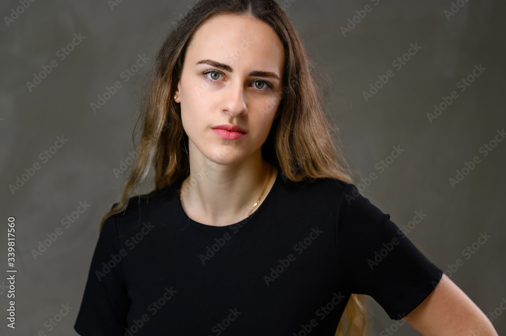 Horizontal portrait of a caucasian girl in a black dress with long hair on a gray background. Horizontal portrait of a caucasian girl in a black dress with long hair on a gray background.