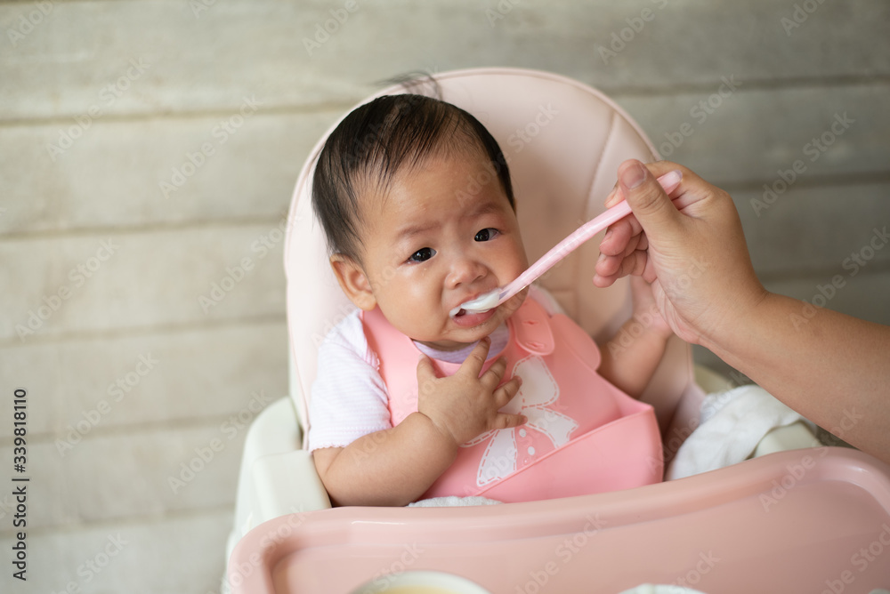 Little newborn baby sitting in baby chair crying and refuses to eat while mother tries to feed with a spoon. Little newborn baby sitting in baby chair crying and refuses to eat while mother tries to feed with a spoon.