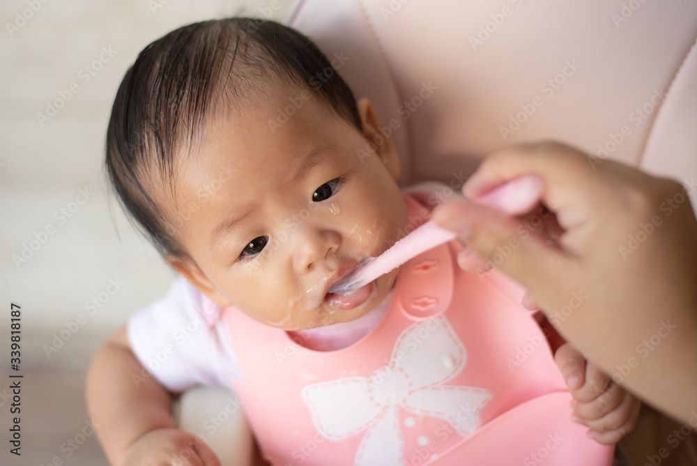 Little newborn baby sitting in baby chair crying and refuses to eat while mother tries to feed with a spoon. Little newborn baby sitting in baby chair crying and refuses to eat while mother tries to feed with a spoon.