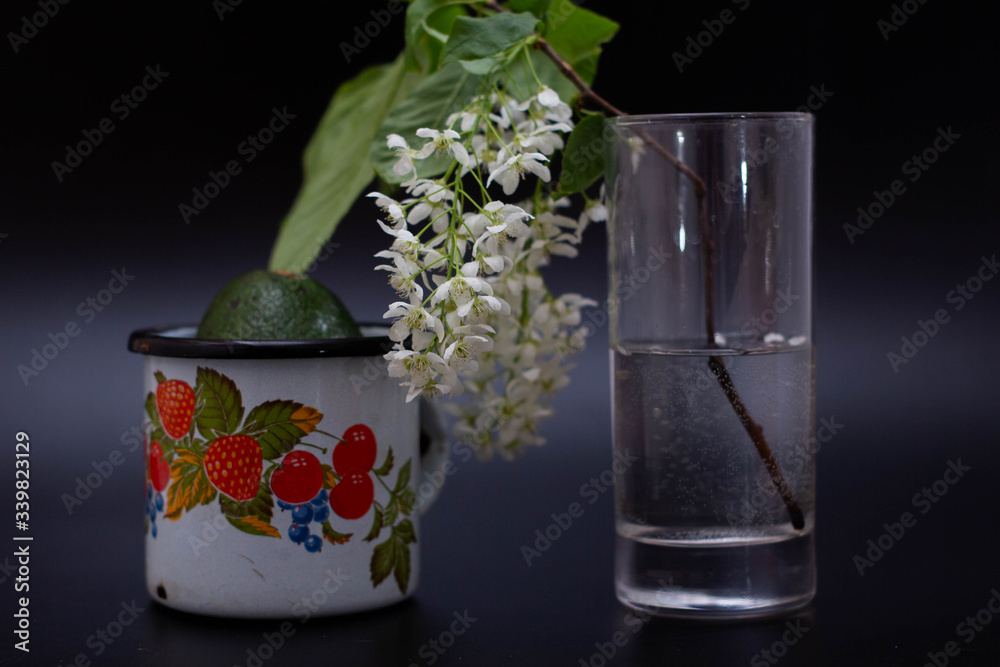 A transparent glass with a flower next to an iron mug with avacado