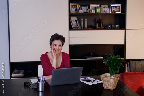 Signora con i capelli scuri e maglia colorata lavora in modalità smart working da casa sua  photo