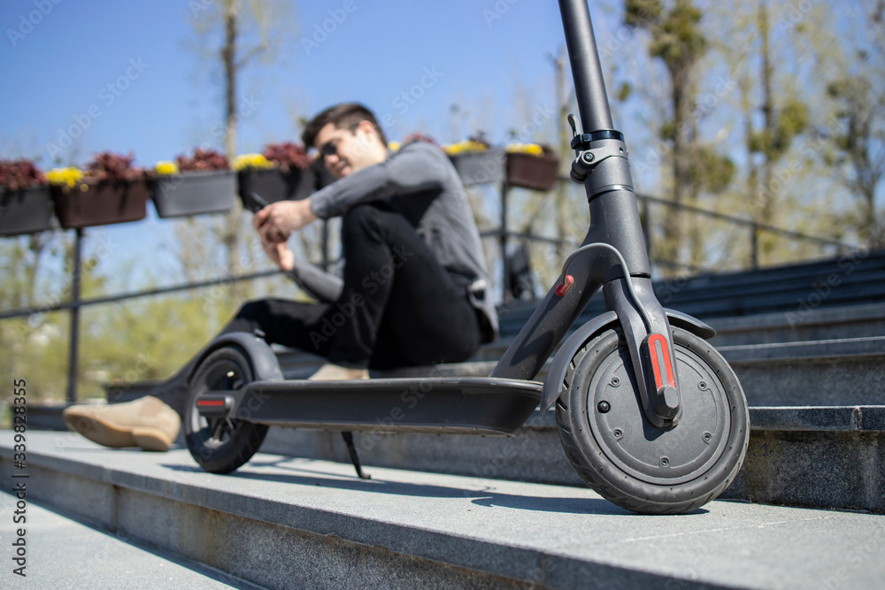 Electric scooter commuting vehicle and young man sitting in background using smart phone.