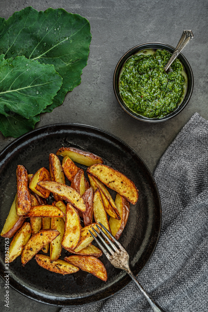 Kartoffelspalten mit Pesto aus Kohlrabiblättern auf einem dunklen Hintergrund