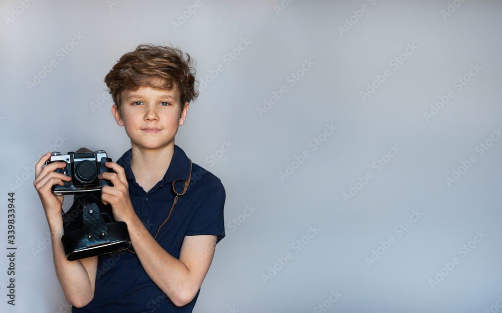 Blond teenager with forelock holding a retro camera on the light blue background Blond teenager with forelock holding a retro camera on the light blue background