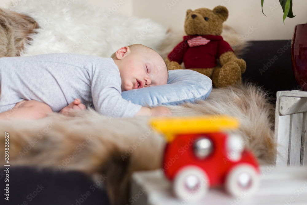Little baby boy sleeping on a sofa on artificial fur, among toys - teddy bears and fire truck Little baby boy sleeping on a sofa on artificial fur, among toys - teddy bears and fire truck