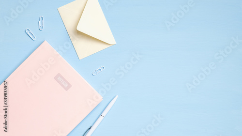 Flat lay, top view modern office desk. Minimal student workspace with pink notebook, envelope, pen, stationery on blue background. Education concept
