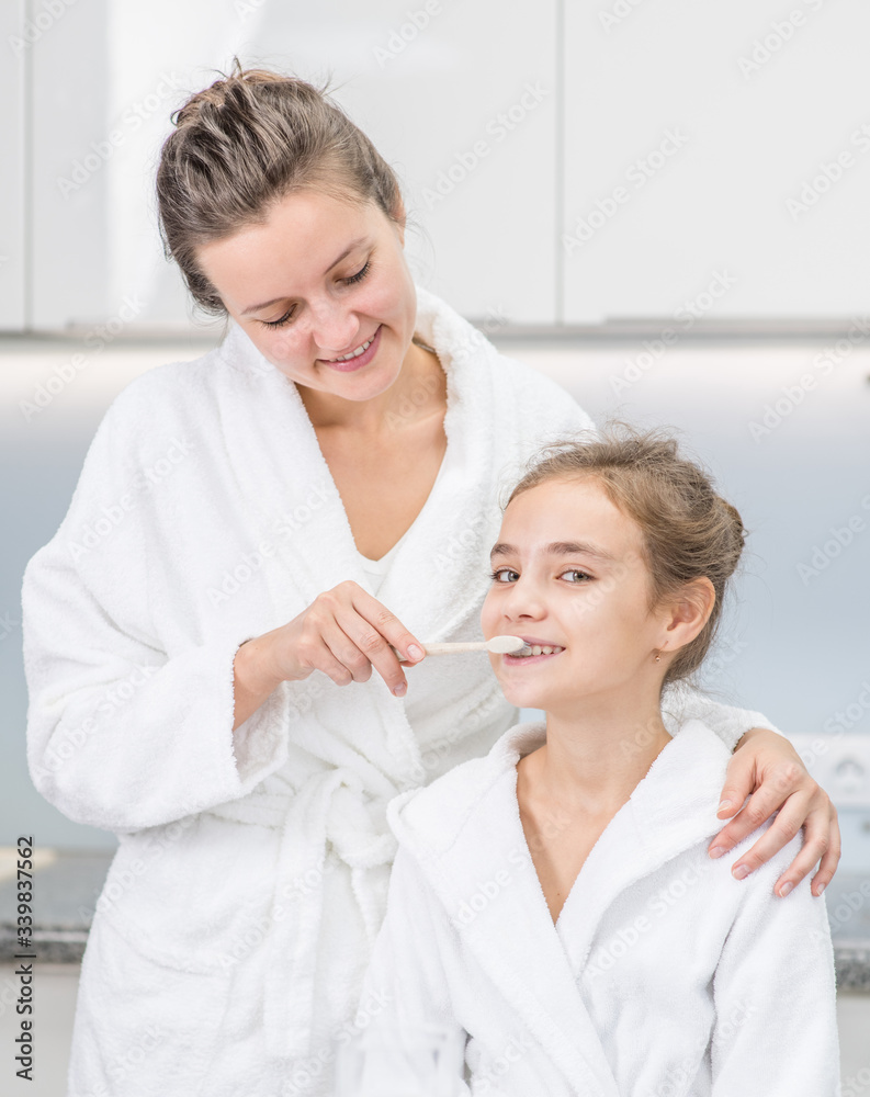 Happy family at home. Smiling mom teaching her young daughter how to brush teeth with toothbrush Happy family at home. Smiling mom teaching her young daughter how to brush teeth with toothbrush