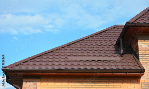 A close-up on a roofing construction covered with metal roof tiles with a snow guard, snow stopper agains blue sky.