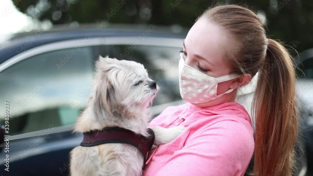 A young woman in a fabric face mask holding her little dog. Covering face in public is recommended by CDC in many countries during to Covid-19 coronavirus pandemic. A young woman in a fabric face mask holding her little dog. Covering face in public is recommended by CDC in many countries during to Covid-19 coronavirus pandemic.