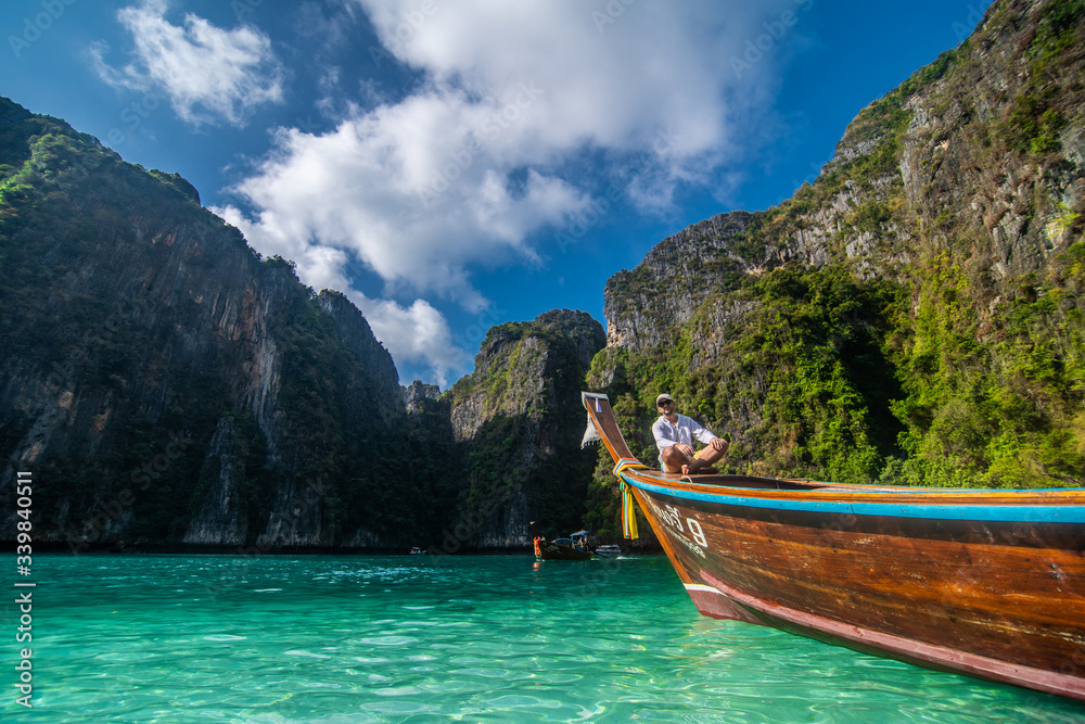 Handsome male cruising on retro wood boat by Andaman sea and behind him you can see Ko Phi Phi Lee Island.