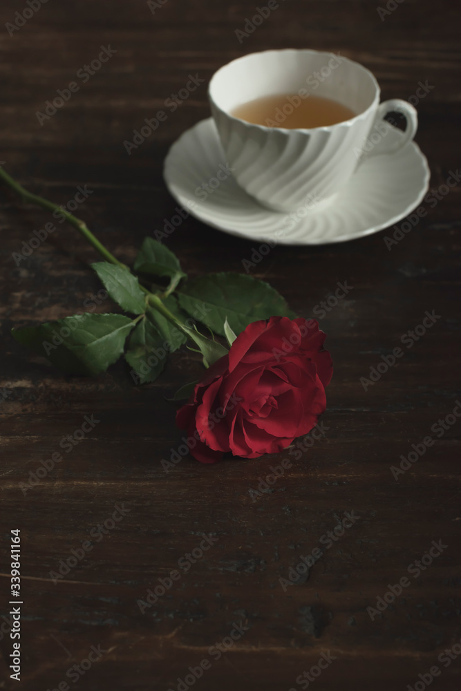 White china tea cup and saucer with red rose on wooden table. White china tea cup and saucer with red rose on wooden table.