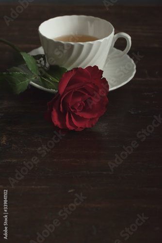 White china tea cup and saucer with red rose on wooden table.