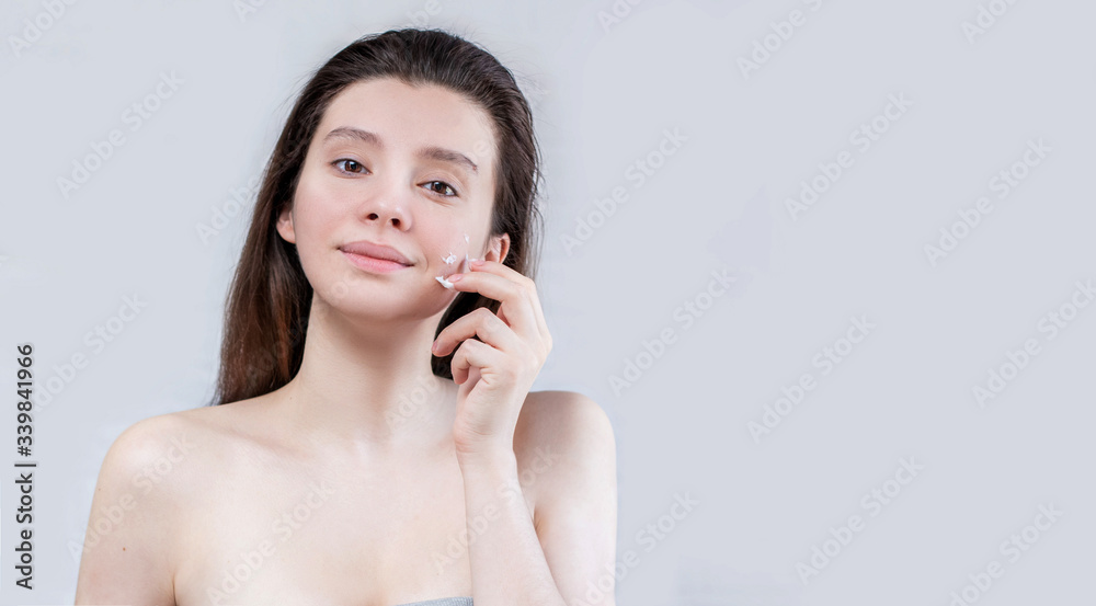 Beautiful young woman applying cream treatment on her face isolated in the background. Clean, fresh skin. Spa and cosmetology Facials for women. The cream is in her hands and touches her face. Beautiful young woman applying cream treatment on her face isolated in the background. Clean, fresh skin. Spa and cosmetology Facials for women. The cream is in her hands and touches her face.