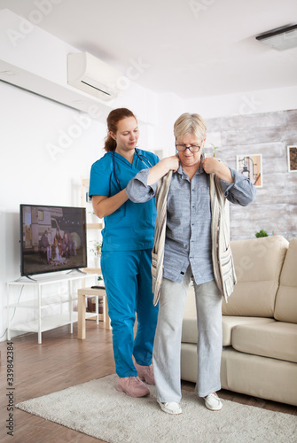 Cuadro en lienzo Young female nurse helping senior woman to get dressed