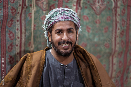 Portrait of Bedouin man wearing traditional clothes praying with a tasbih while drinking tea on a carpet in the Saudi desert