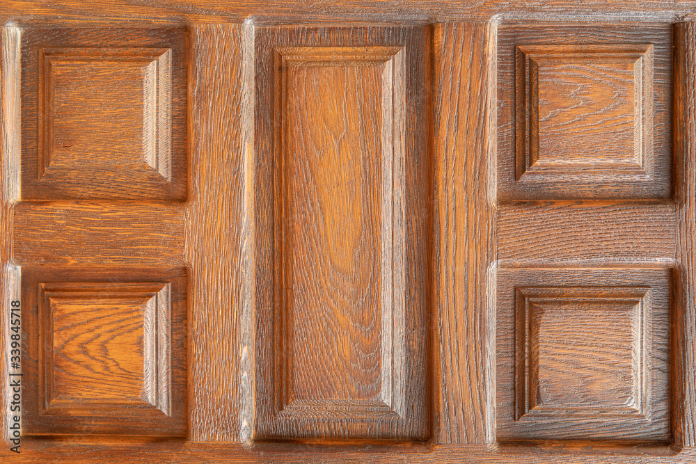 Close-up on a wooden door showing repetitive patterns due to precise craftsmanship. The patterns are square and rectangular and have several levels of depth Close-up on a wooden door showing repetitive patterns due to precise craftsmanship. The patterns are square and rectangular and have several levels of depth
