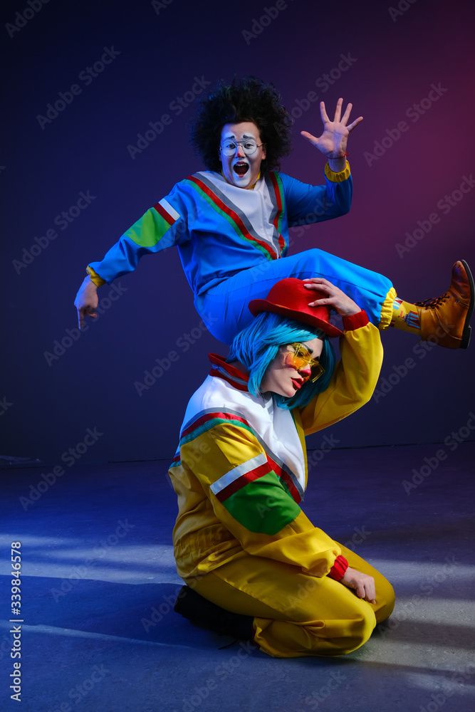 Two clowns a man and a woman with makeup in bright colored tracksuits in the style of the 80s.