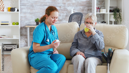 Female doctor sitting on sofa with senior woman in nursing home giving her daily pills photo