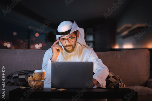 Fototapet Arab man working from home sitting on sofa late at night time