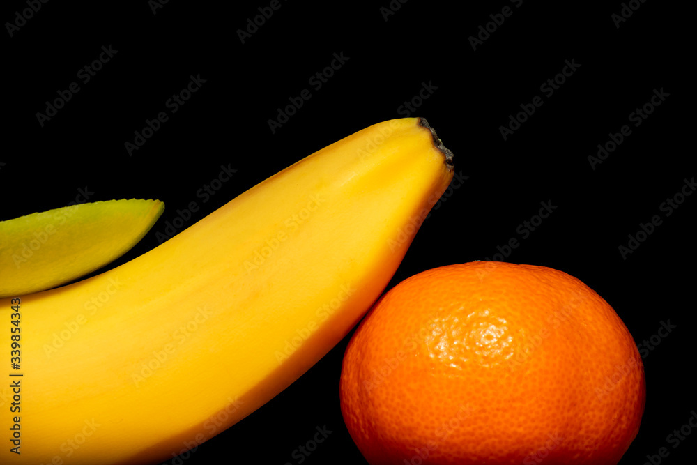 Banana, mandarin and slice apple on a black background