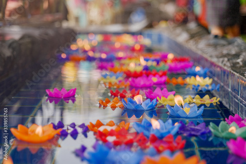 Close up view, lotus flower candles with flame among floating colourful flower on water for worship buddha in Thai temple. Pray for buddha in traditional Asian culture. 