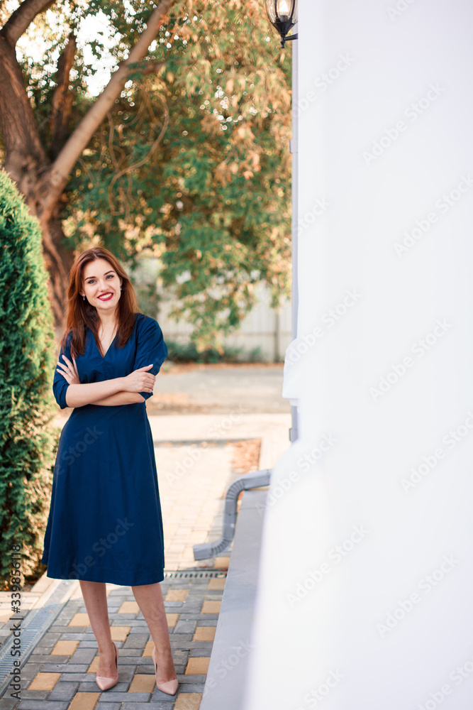 Red-haired model in a dark blue dress posing in the garden. Red-haired model in a dark blue dress posing in the garden.