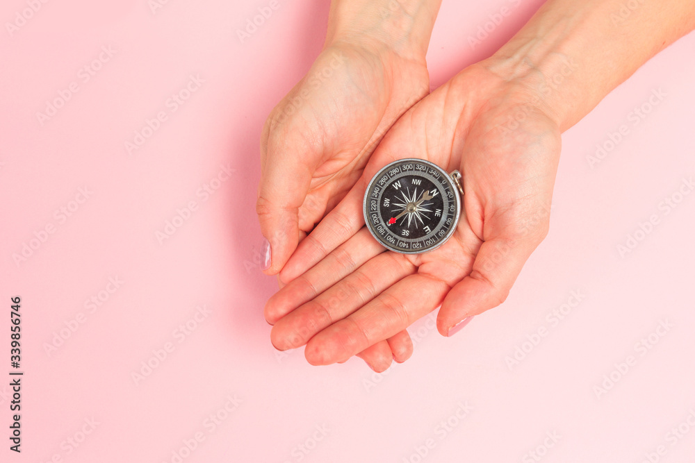 Beautiful young woman's hands holding compass on pastel pink background. Beautiful young woman's hands holding compass on pastel pink background.