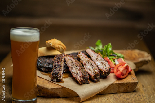 Smoked pork ribs with tomatoes, salad and bread on wood cutting board with glass of beer
