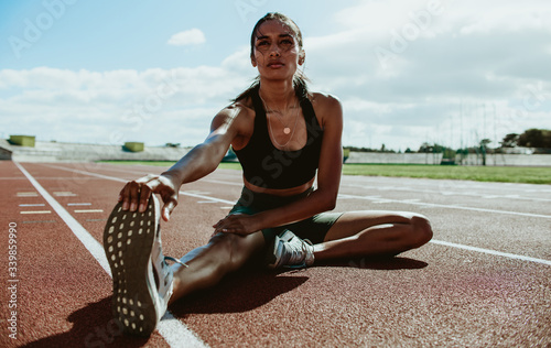 Fototapeta Naklejka Na Ścianę i Meble -  Female runner doing stretching exercises sitting on the track