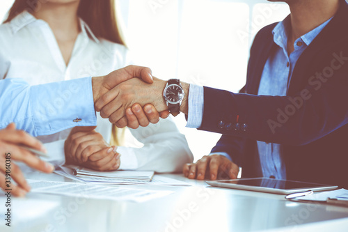 Business people shaking hands at meeting or negotiation, close-up. Group of unknown businessmen and women in modern office. Teamwork, partnership and handshake concept, toned picture