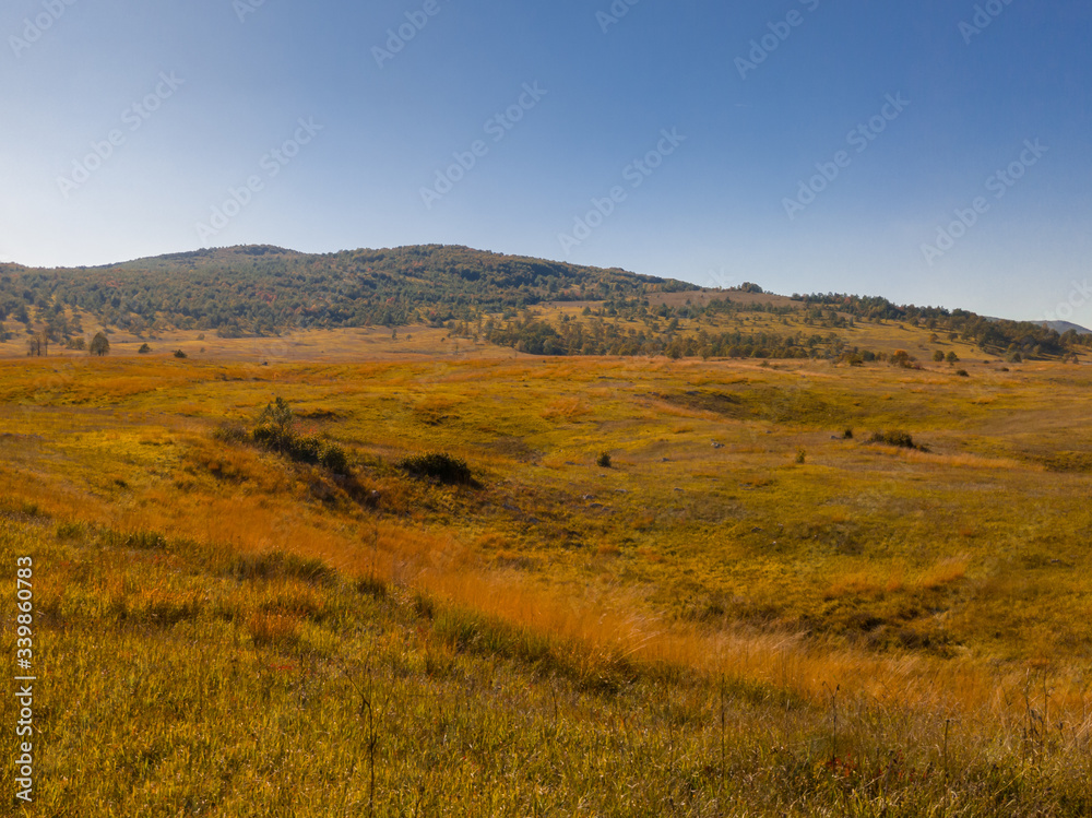 Autumn on the Klekovaca mountain near Bosanski Petrovac. Fall colors in the countryside. Mountain landscape. Grassy rural slopes with fields and trees in fall foliage in autumn.