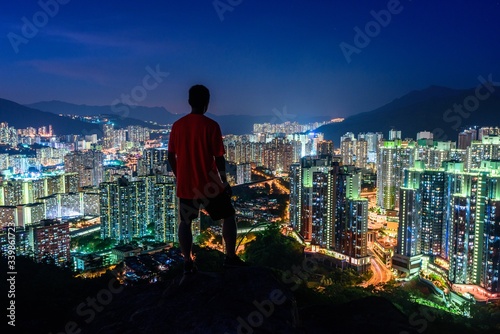 Photography Person standing on a cliff looking over the lighted skyscrapers at night capture