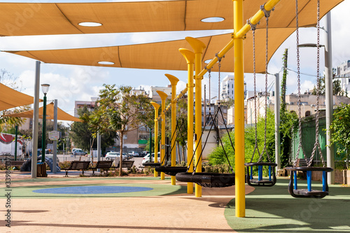 Empty yellow playground, black swings and benches. No children, parents, no people. Sunny weather,park,warm. Virus and quarantine. The concept of protecting and preventing viruses and epidemics. Urban