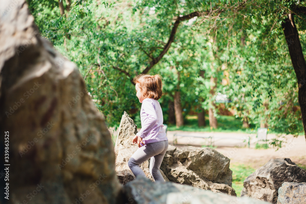 A little girl in a t-shirt and pants climbs on rocks, mountains, peaks, conquering peaks, game, Park, forest, adventure with family, learning geography, terrain