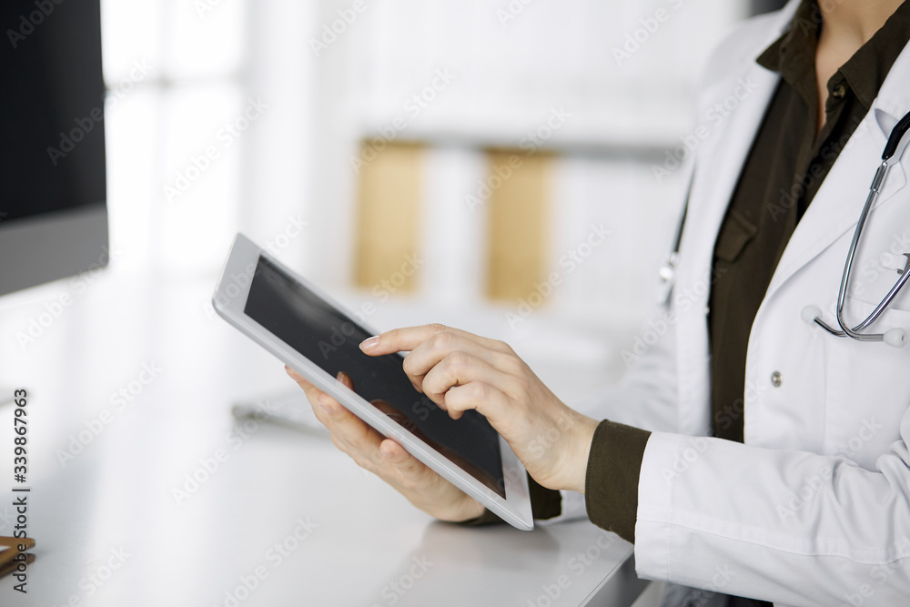 Unknown female doctor using tablet computer in clinic. Perfect medical service in hospital. Medicine concept Unknown female doctor using tablet computer in clinic. Perfect medical service in hospital. Medicine concept