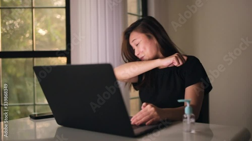 Asian woman sneeze and cough having serious symptoms of coronavirus. Working from home and social distancing. Hand gel sanitizer on the table for protection. Workspace from home.