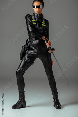 attractive futuristic african american woman in glasses with sword on grey