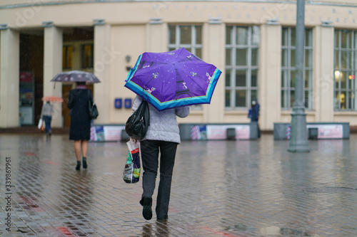 Photography of a woman hurrying in the rain. She is hiding under an umbrella. Wet city street. Way to the subway. Almost no people. Coronavirus pandemic lifestyles. photo