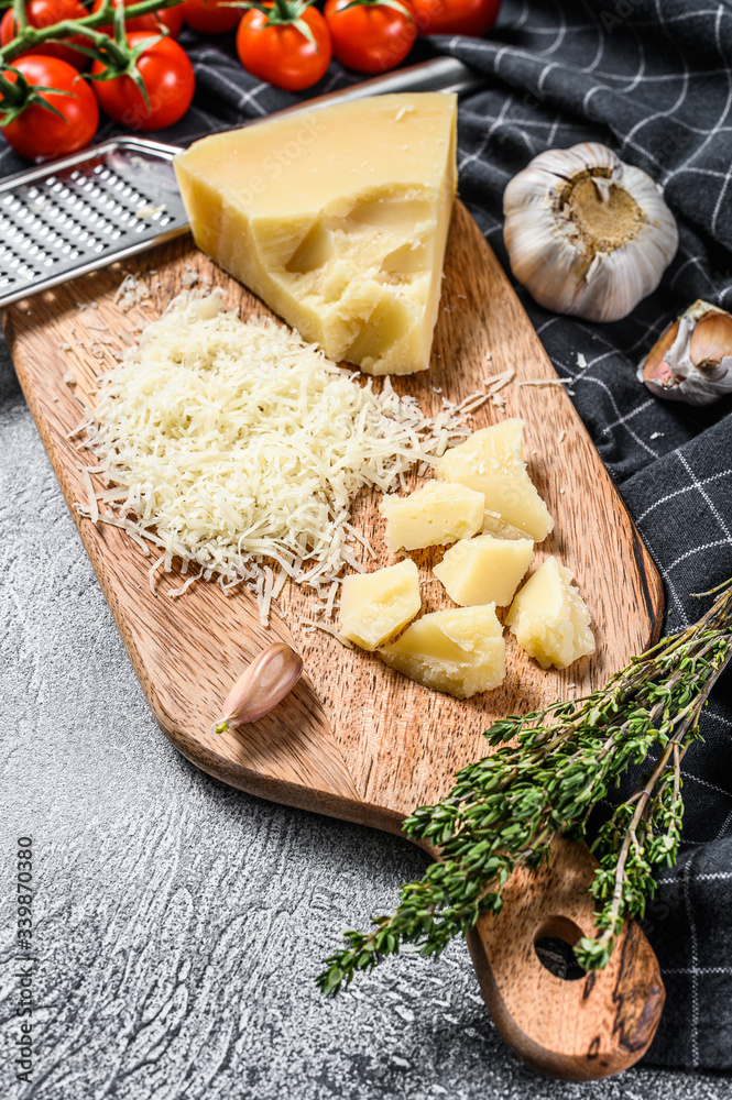 Grated parmigiano reggiano cheese and metal grater on wooden cutting board.  Gray background. Top view