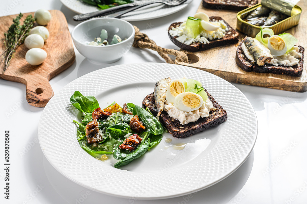 Sandwiches with sardines, egg, cucumber and cream cheese, salad garnish with spinach and dried tomatoes. White background. Top view