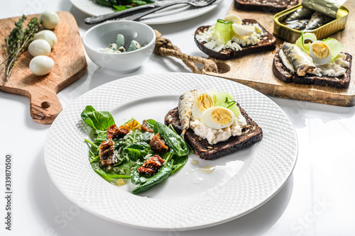 Sandwiches with sardines, egg, cucumber and cream cheese, salad garnish with spinach and dried tomatoes. White background. Top view