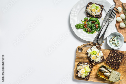 Sandwiches with sardines, egg, cucumber and cream cheese, salad garnish with spinach and dried tomatoes. White background. Top view. Copy space